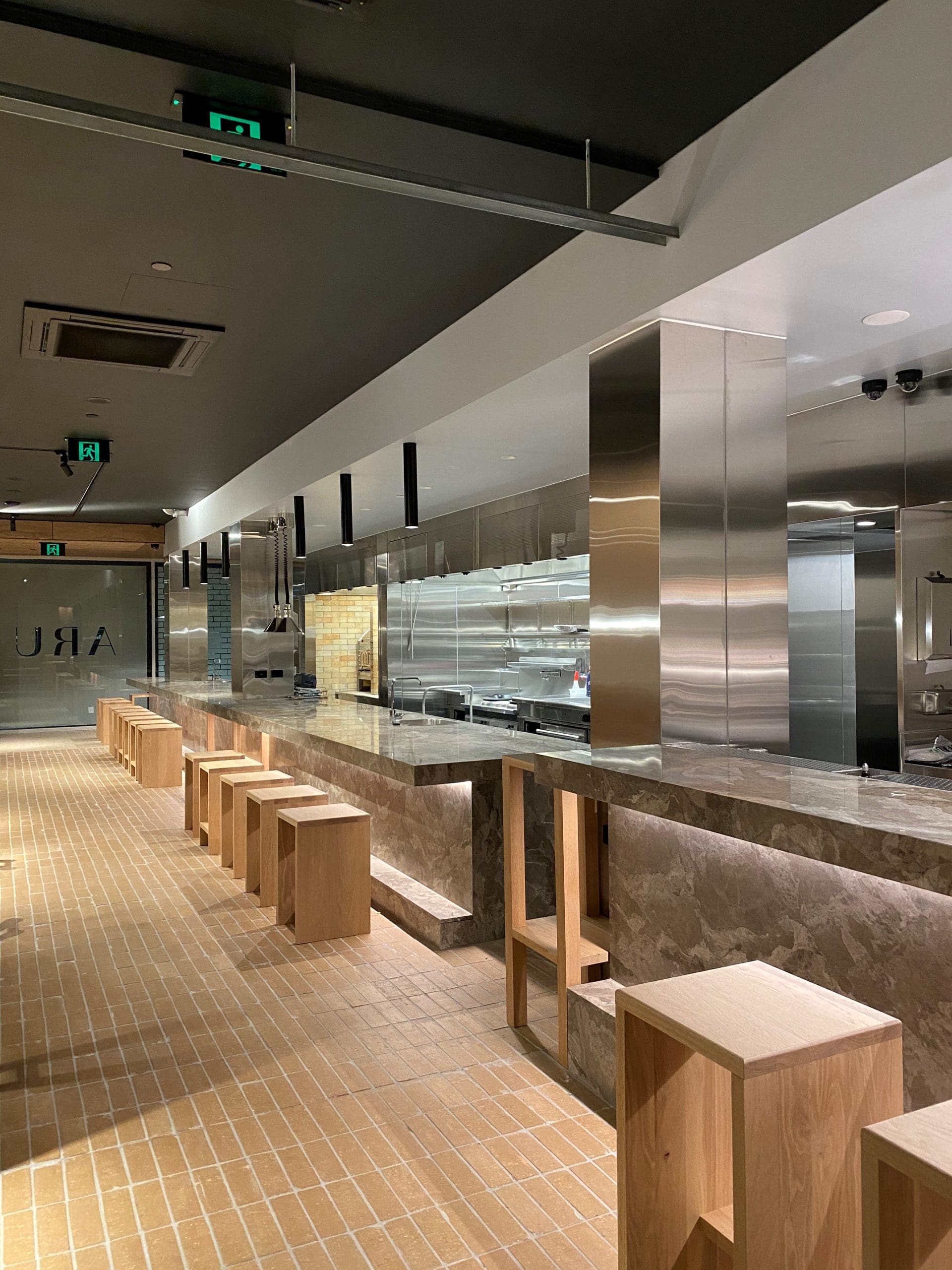 Restaurant interior at Aru showcasing a sleek design with kitchen marble benchtops and modern wooden seating along a polished, open kitchen.